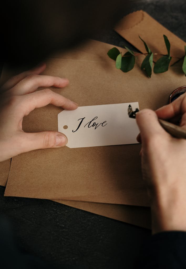 Hands crafting a handwritten 'I love' note with elegant calligraphy style.